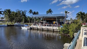 A waterfront restaurant with outdoor seating, boats docked nearby, and palm trees in the background. - Keys stilt cottage lower unit (Naples)