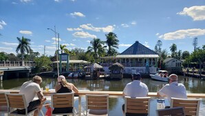 A waterfront restaurant with outdoor seating, a thatched-roof structure, and a view of the water and boats. - Keys stilt cottage lower unit (Naples)