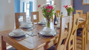 A dining area with a wooden table set for six, including plates, glasses, and cutlery. There are two vases with flowers on the table. - 5 bedroom accommodation in Glandwr, near Narbeth (Glandwr, near Narbeth)