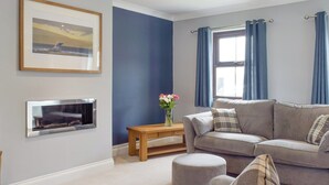 A living room with a grey sofa, a wooden coffee table, a fireplace, and a window with blue curtains. - 5 bedroom accommodation in Glandwr, near Narbeth (Glandwr, near Narbeth)