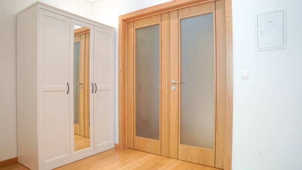 Een kamer met een houten garderobe, een witte garderobe en een houten deur met geëtste glaspanelen.