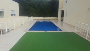 A swimming pool with a green deck area, surrounded by white railings and a beige building. - Vacation Home 2 Bedroom Luxury Home With Pool in Patroves (Albufeira)