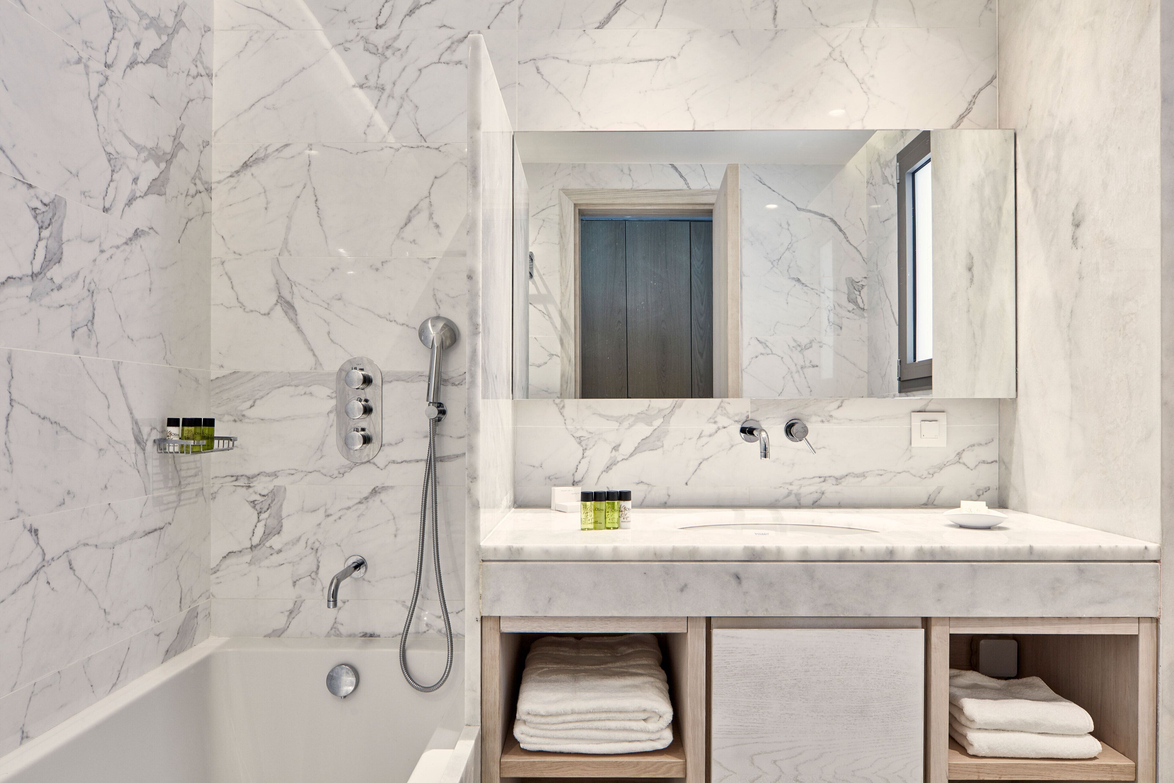Een moderne badkamer met een marmeren wand, een ingebouwd wastafelmeubel, een spiegel en een douche.
