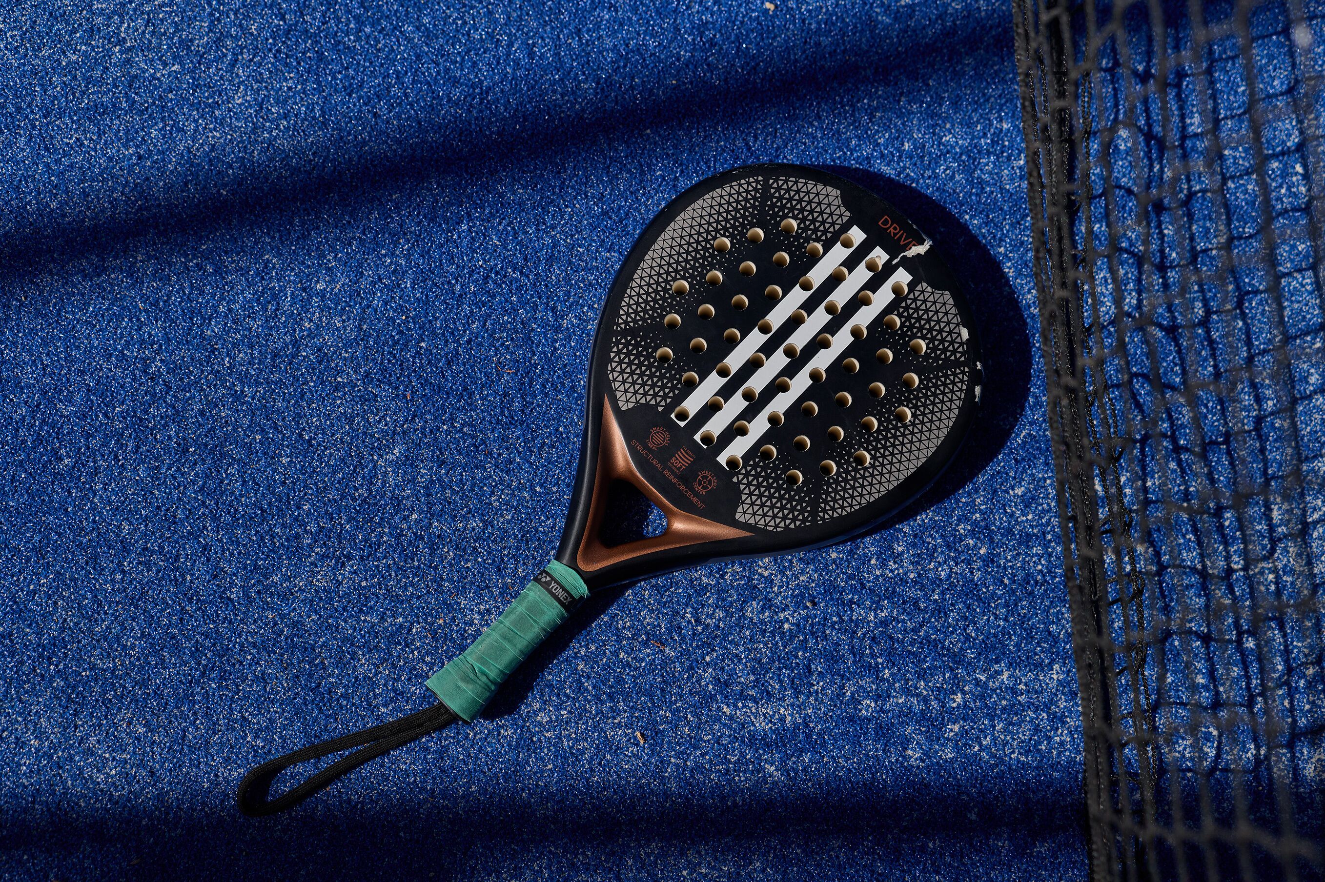 A tennis racket with a textured grip and a green accent, lying on a blue textured surface.