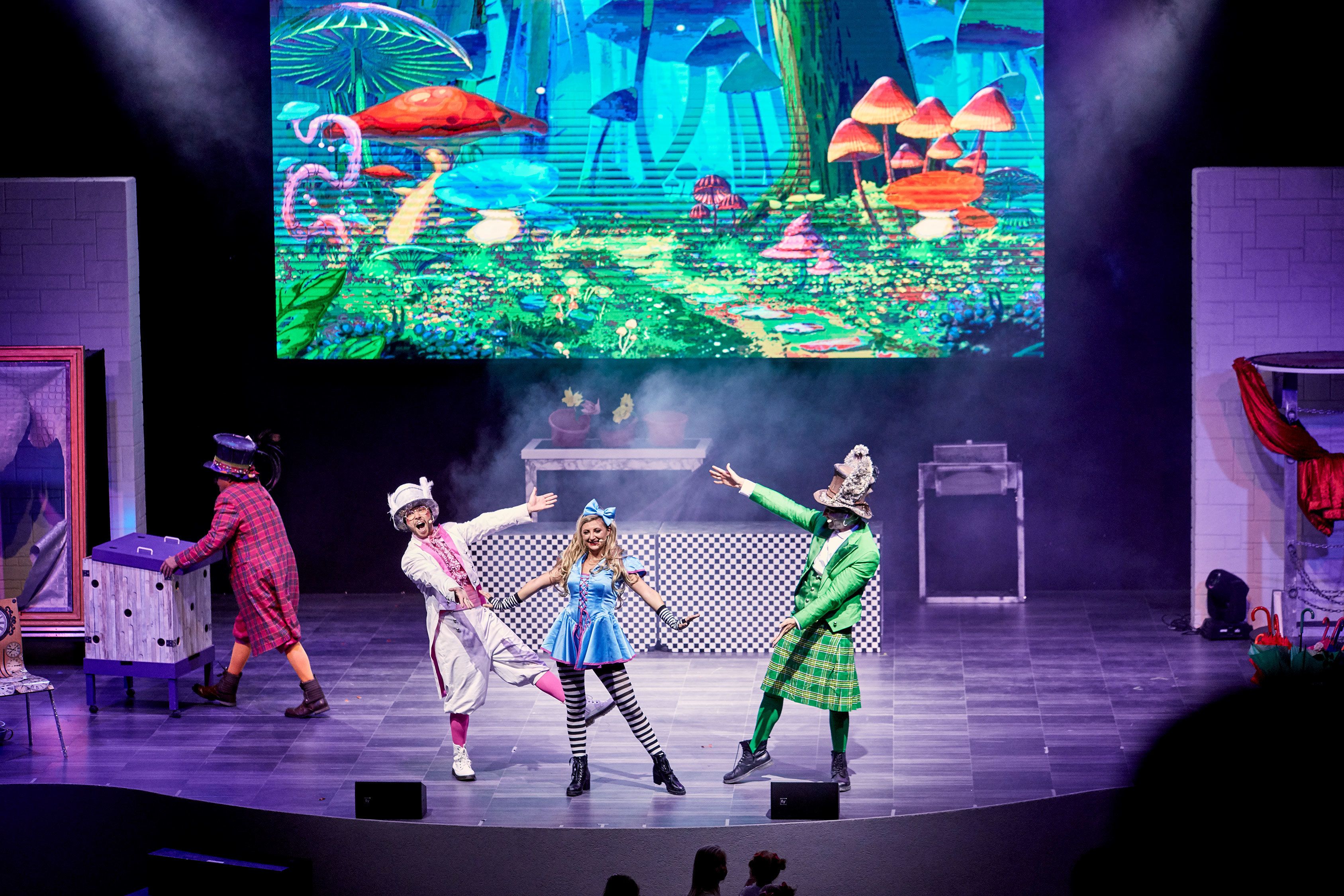 A stage with performers in costumes, a large screen displaying a colorful scene, and a checkered floor.