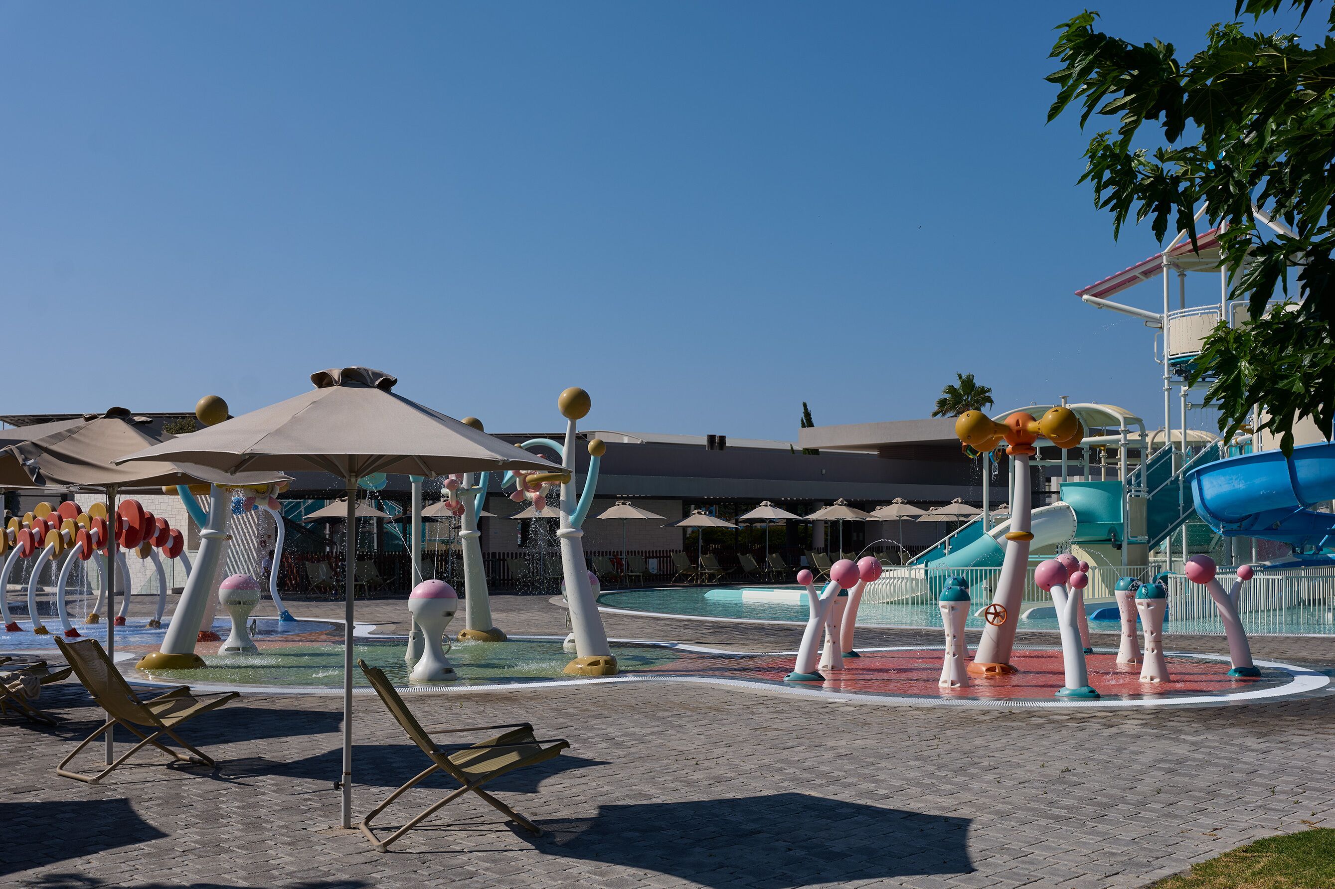 Zona de parque acuático con toboganes, fuentes y sillones de descanso.