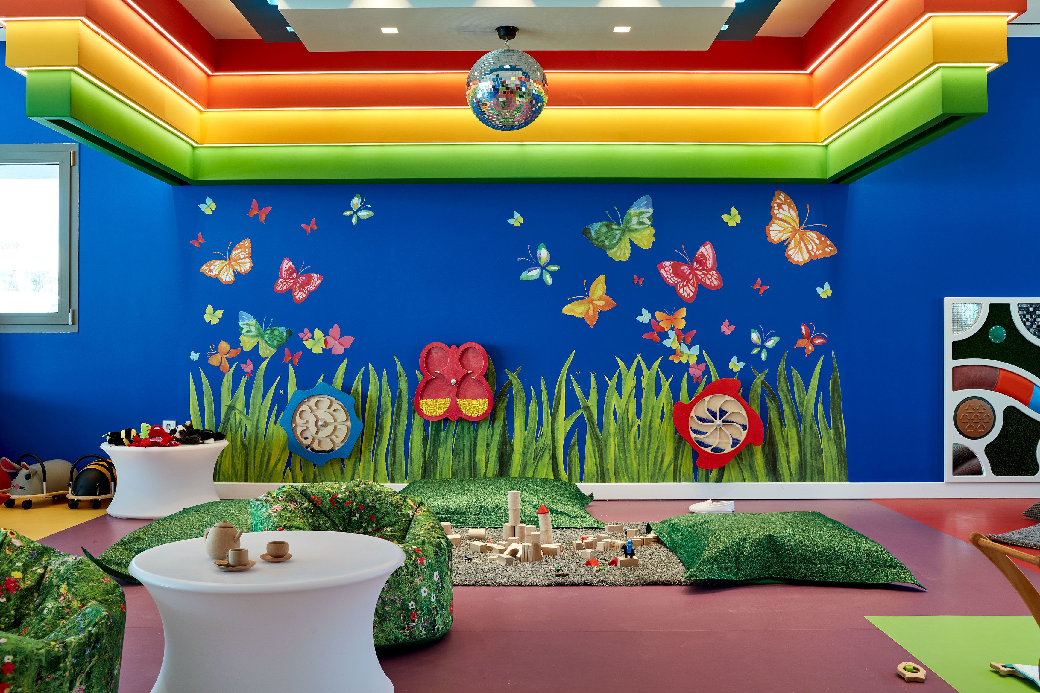 A vibrant children's playroom with colorful walls, a disco ball, and a play area with toys and a green carpet.