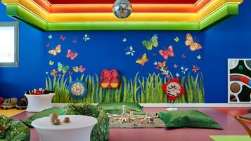 A vibrant children's playroom with colorful walls, a disco ball, and a play area with toys and a green carpet.