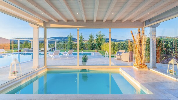 A modern indoor pool area with clear glass walls, a view of the outdoors, and a wooden ceiling.