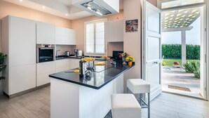 A modern kitchen with a central island, built-in appliances, and a view to a garden through an open door.