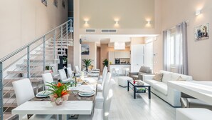 A modern living room with a staircase, a dining area, and a kitchen.