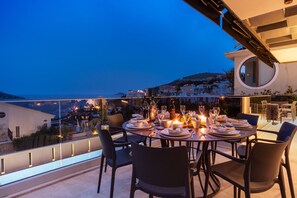 A rooftop dining area with a table set for four, overlooking a coastal town at dusk. - Super Modern 5 Bedroom Villa, Private Pool and Roof Terrace  (Kalkan mahallesi)