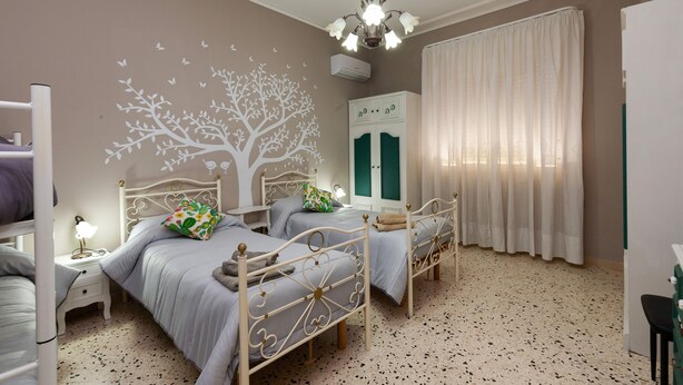 A bedroom with two beds, a tree mural, a ceiling light, and a window with curtains. - Elegant apartment located in the heart of Palermo, equipped with all comforts. (Palermo)