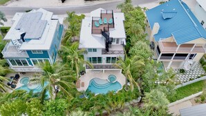A multi-story residential building with a rooftop deck, a swimming pool, and lush tropical landscaping.