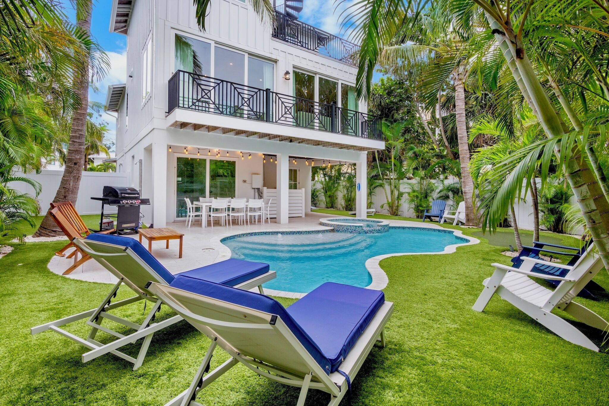 Et moderne hus i to etager med swimmingpool, udendørs møbler og frodig vegetation.