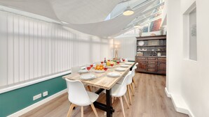 A dining area with a wooden table set for six, white chairs, and a white ceiling shade. - Bakers House, Wells Next Sea (Norfolk)