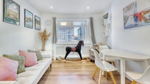 A modern living room with a sofa, a rocking horse, a dining table with chairs, and a window with a view of buildings. - Bakers House, Wells Next Sea (Norfolk)
