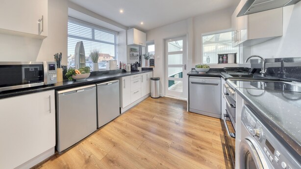 A modern kitchen with white cabinetry, stainless steel appliances, and a wooden floor. - Bakers House, Wells Next Sea (Norfolk)