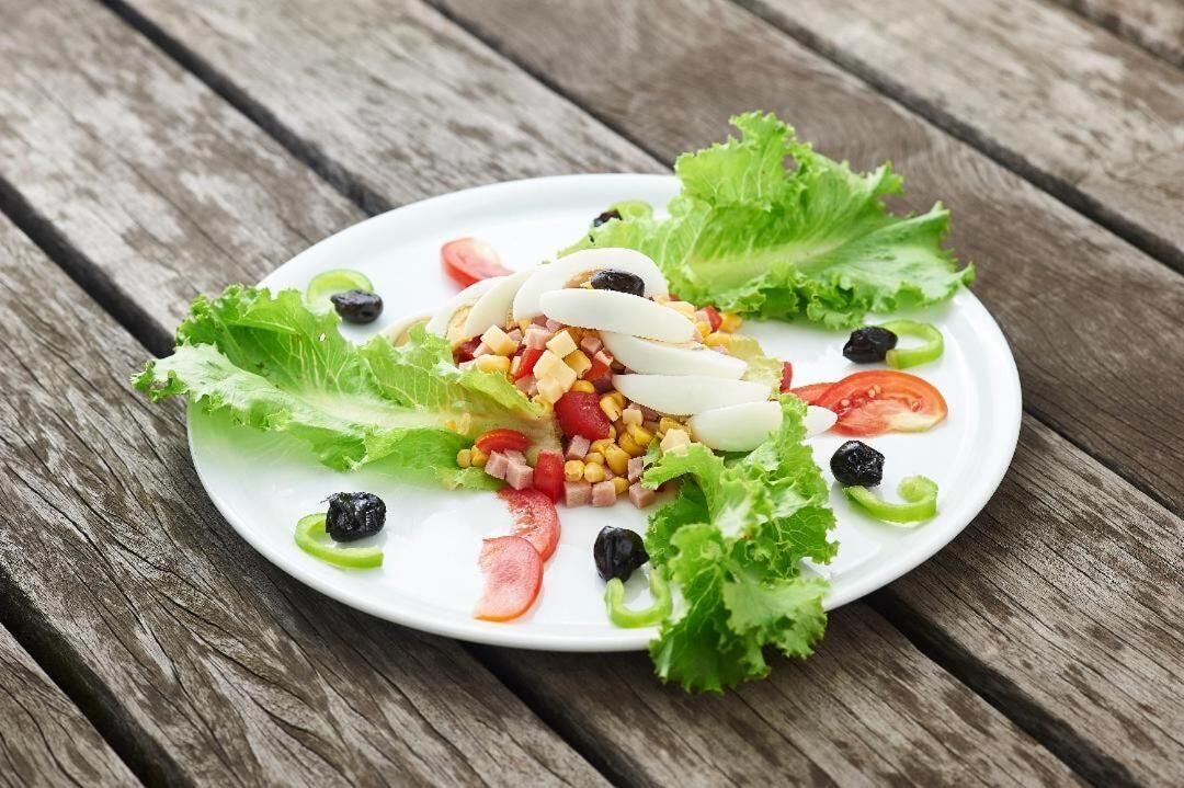 A white plate with a salad on a wooden table.