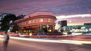 A multi-story building with a curved facade, a covered outdoor seating area, and a parking lot with light trails indicating traffic. - Kactus  Lodge (Pointe-Noire)
