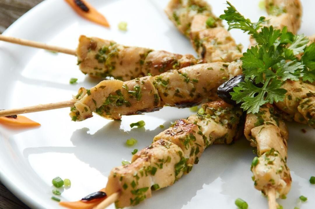 Skewers of grilled chicken garnished with herbs and parsley on a white plate.