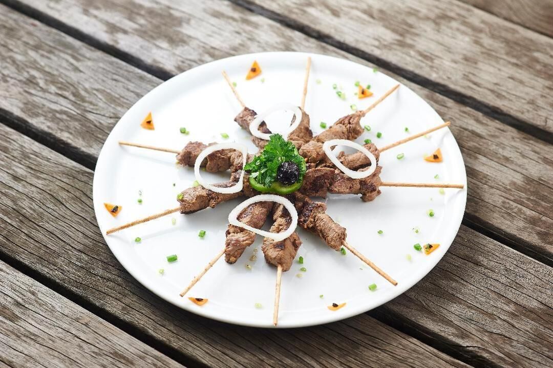 A white plate with skewered meat garnished with onions and green herbs, placed on a wooden surface.
