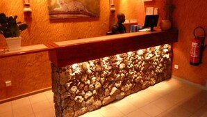 A reception area with a stone wall, a reception desk, a computer monitor, and a fire extinguisher. - Kactus  Lodge (Pointe-Noire)