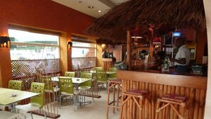 A restaurant with a thatched roof, green chairs, and a bar area. - Kactus  Lodge (Pointe-Noire)