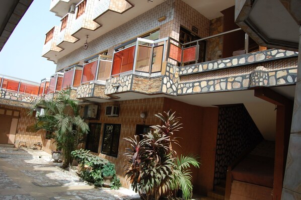 A multi-story building with a stone facade, multiple balconies with red railings, and a variety of potted plants. - Benin Hotel Terminus (Cotonou)