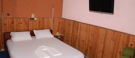 A room with a wooden bed, a television mounted on the wall, and a green armchair.