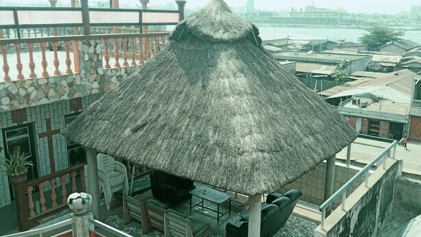 Een gebouw met rieten dak en betegelde vloer, omgeven door een balkon met een hekwerk.