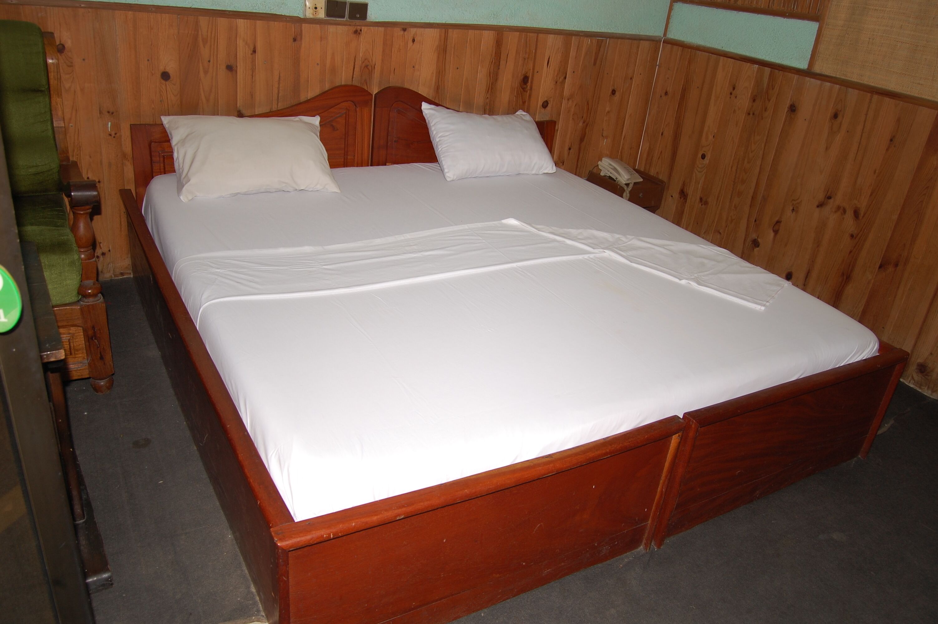Un lit en bois recouvert de draps blancs, dans une pièce aux murs lambrés.