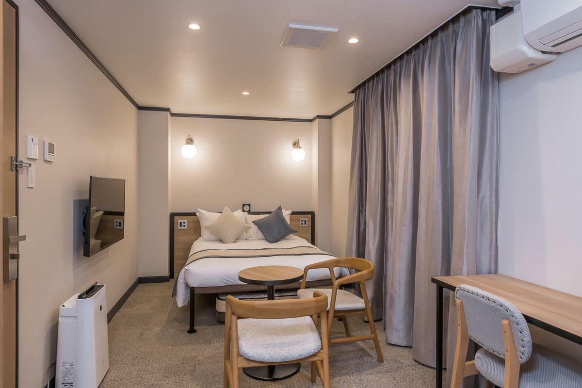 Habitación de hotel con cama, mesita de noche, dos sillones, una mesita redonda, televisión y aire acondicionado.