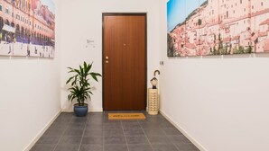 A hallway with a wooden door, a potted plant, a welcome mat, and two framed pictures on the walls. - Juliette Rooms (Jesi)