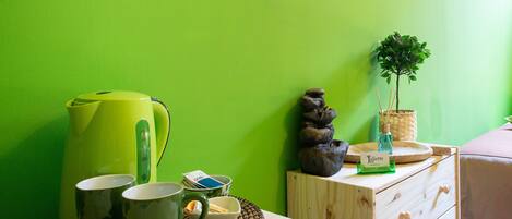 Una habitación con pared verde, una mesa de madera con una bandeja que sostiene tazas verdes, una tetera verde y una planta pequeña.