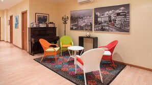 A hotel lobby with a piano, colorful chairs, a patterned rug, and two black-and-white cityscape posters on the wall. - Juliette Rooms (Jesi)