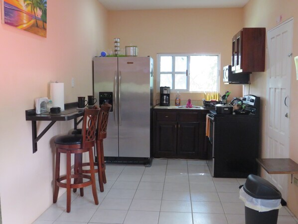 Cozinha compacta com geladeira, pia e um pequeno espaço de refeições com cadeiras.