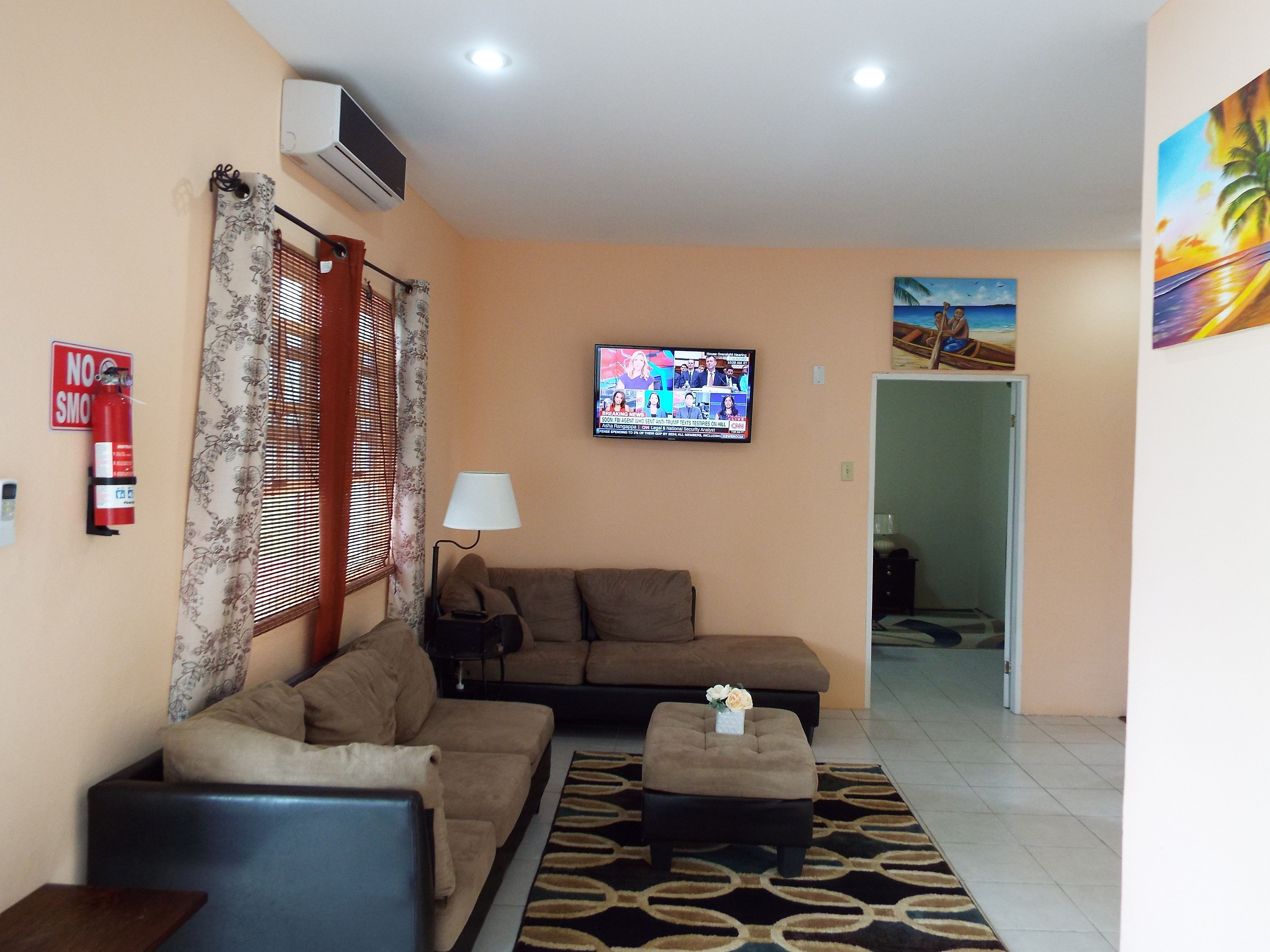 Una sala de estar con sofá, reposapiés y un televisor que muestra un noticiero.