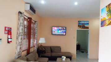 Una sala de estar con sofá, reposapiés y un televisor que muestra un noticiero.