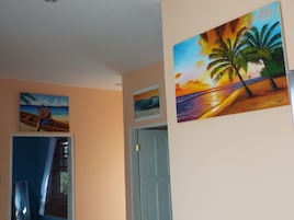 Una habitación con una puerta, un cuadro de una playa al atardecer y una fotografía enmarco de un bote en la playa.