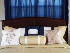 Una cama con cabecera de madera, varios almohadones y una colcha color beige.
