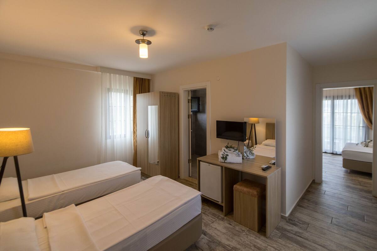 A hotel room with two beds, a desk with a TV, a small fridge, and a lamp.