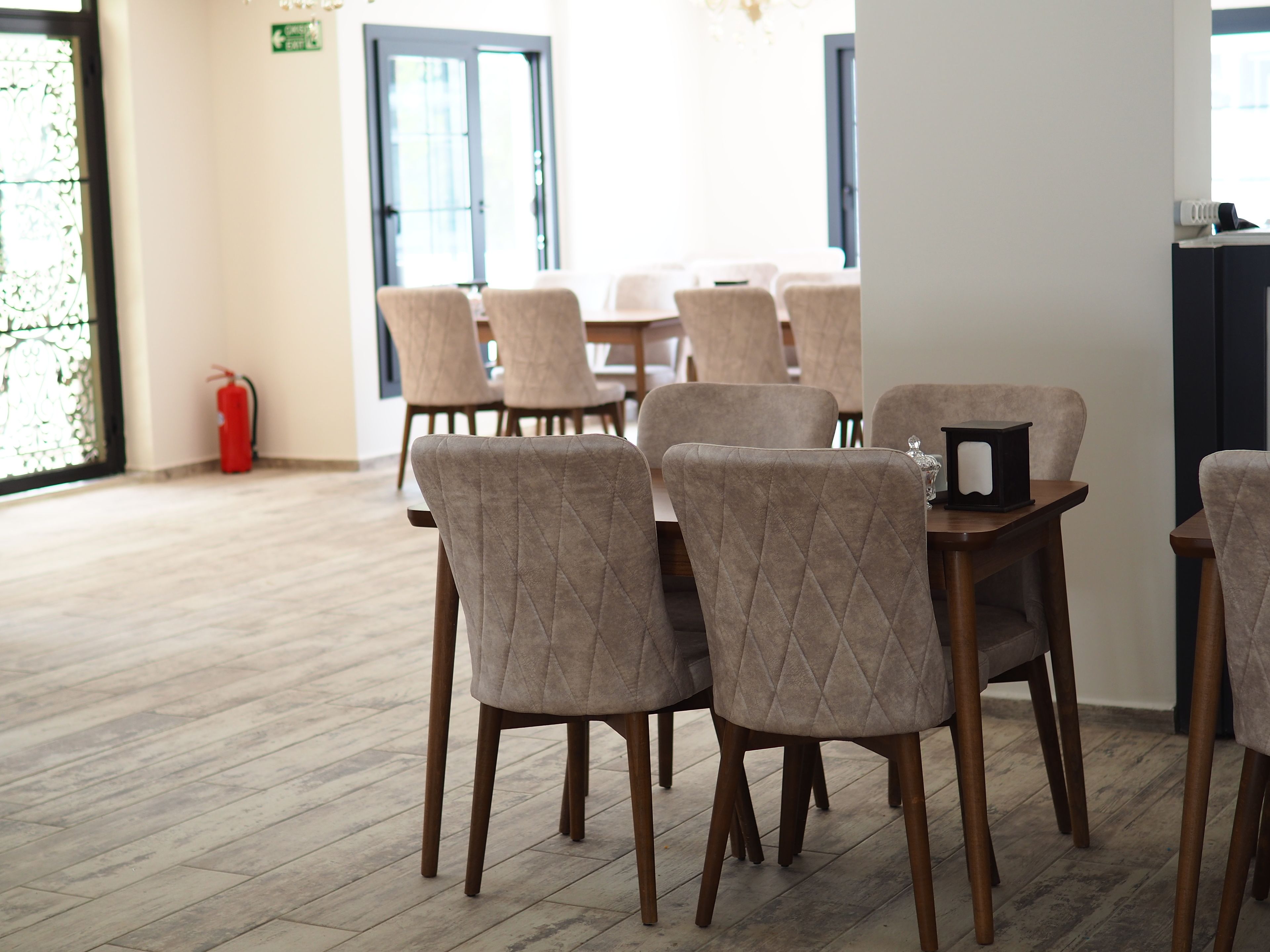 Un comedor con mesas y sillas de madera, un extintor y una ventana con persianas.