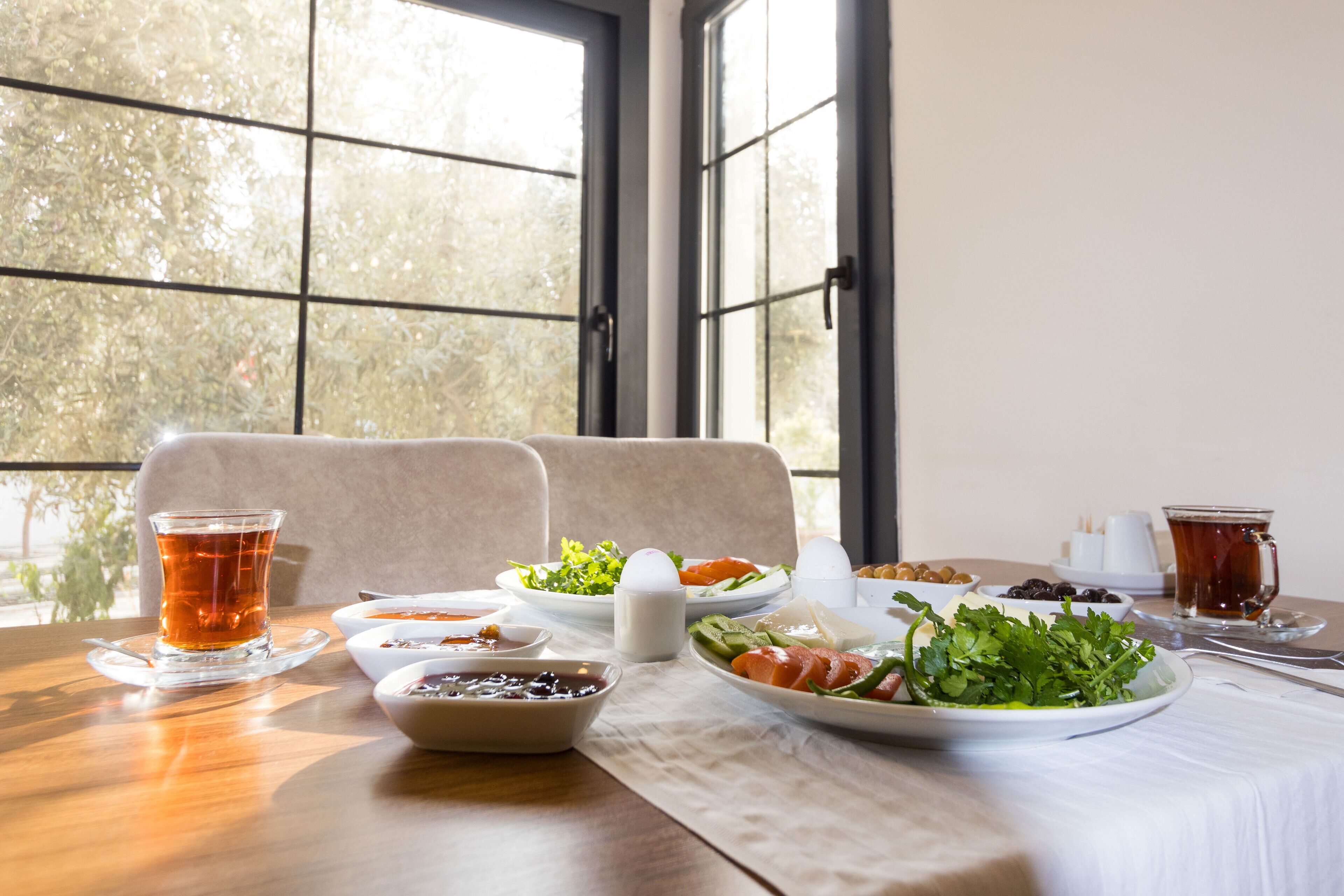 Une table à manger dressée avec différents plats et boissons, placée devant une fenêtre donnant sur un paysage arboré.