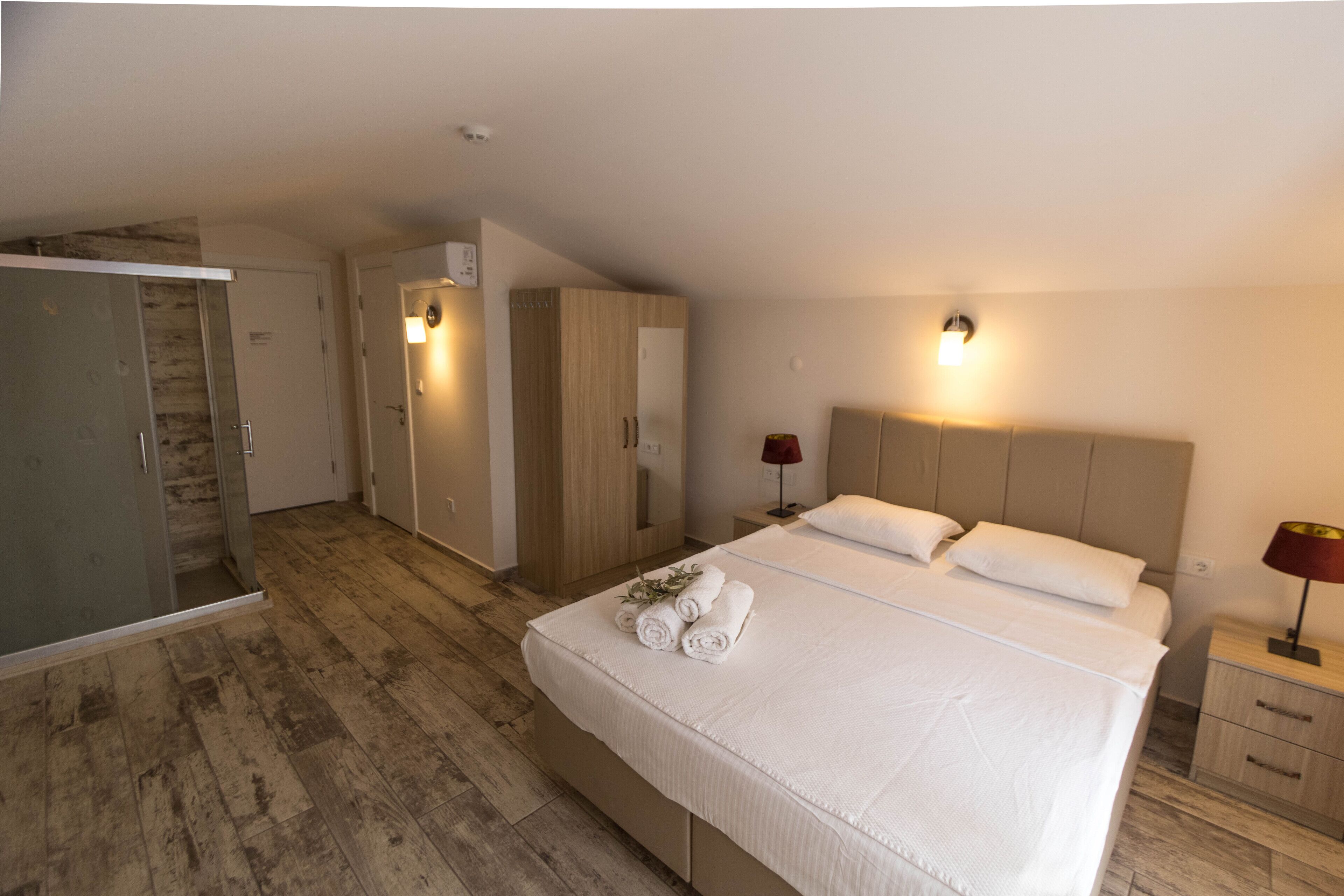 A bedroom with a large bed, a wardrobe, a mirror, and a bedside table with a lamp.