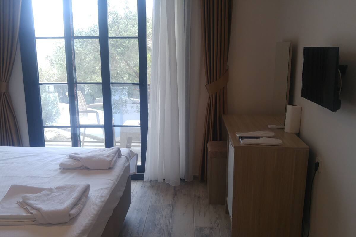 A hotel room with a large bed, a wooden desk, a TV, and a view of the outdoors through a window.