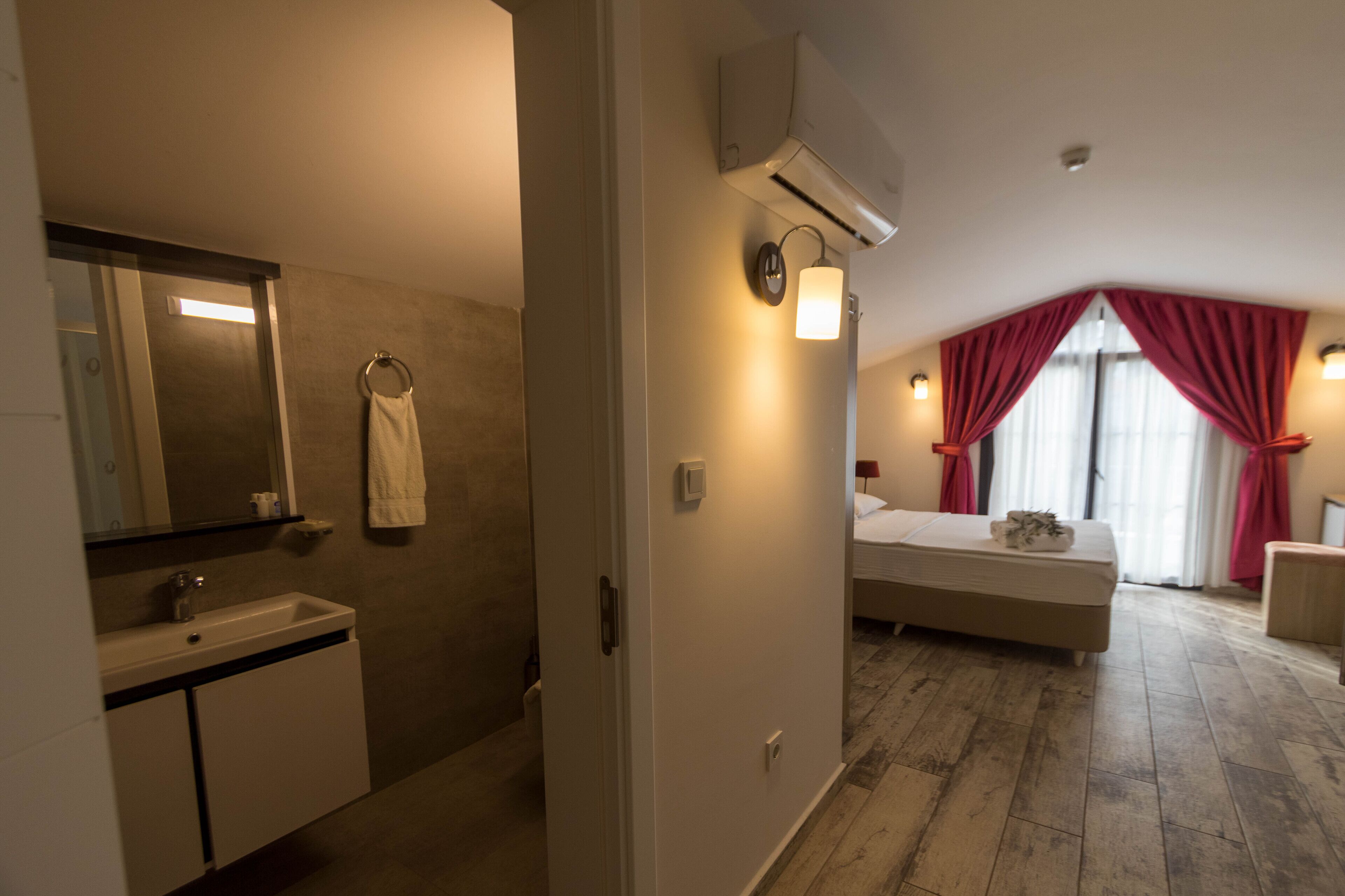 A hotel room with a bathroom, a bed, a nightstand, and a window with curtains.
