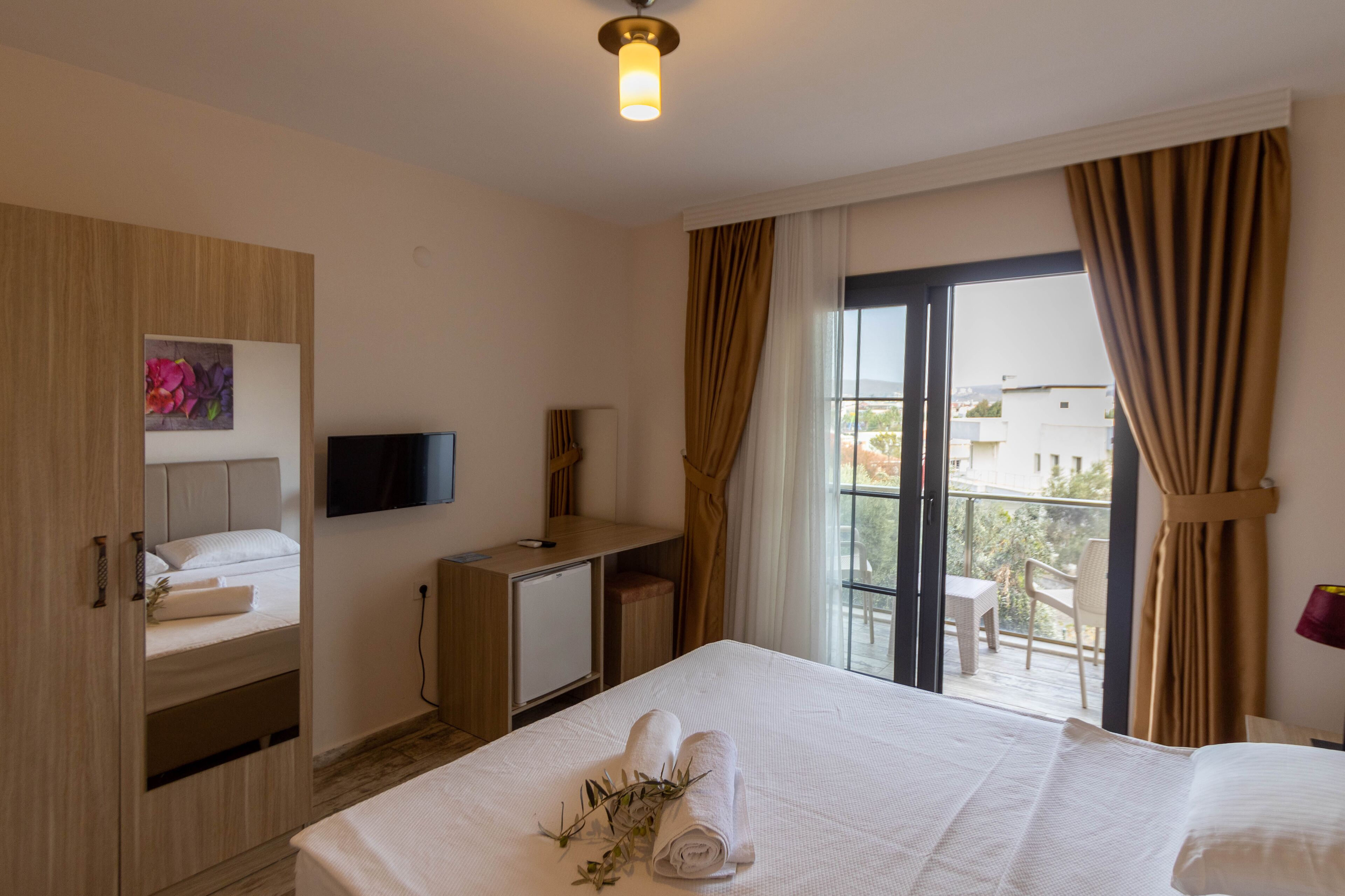 A hotel room with a bed, a desk, a TV, and a balcony with curtains.