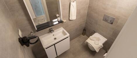 Un baño con lavamanos, espejo, toallero, inodoro y una toalla colgada en la pared.