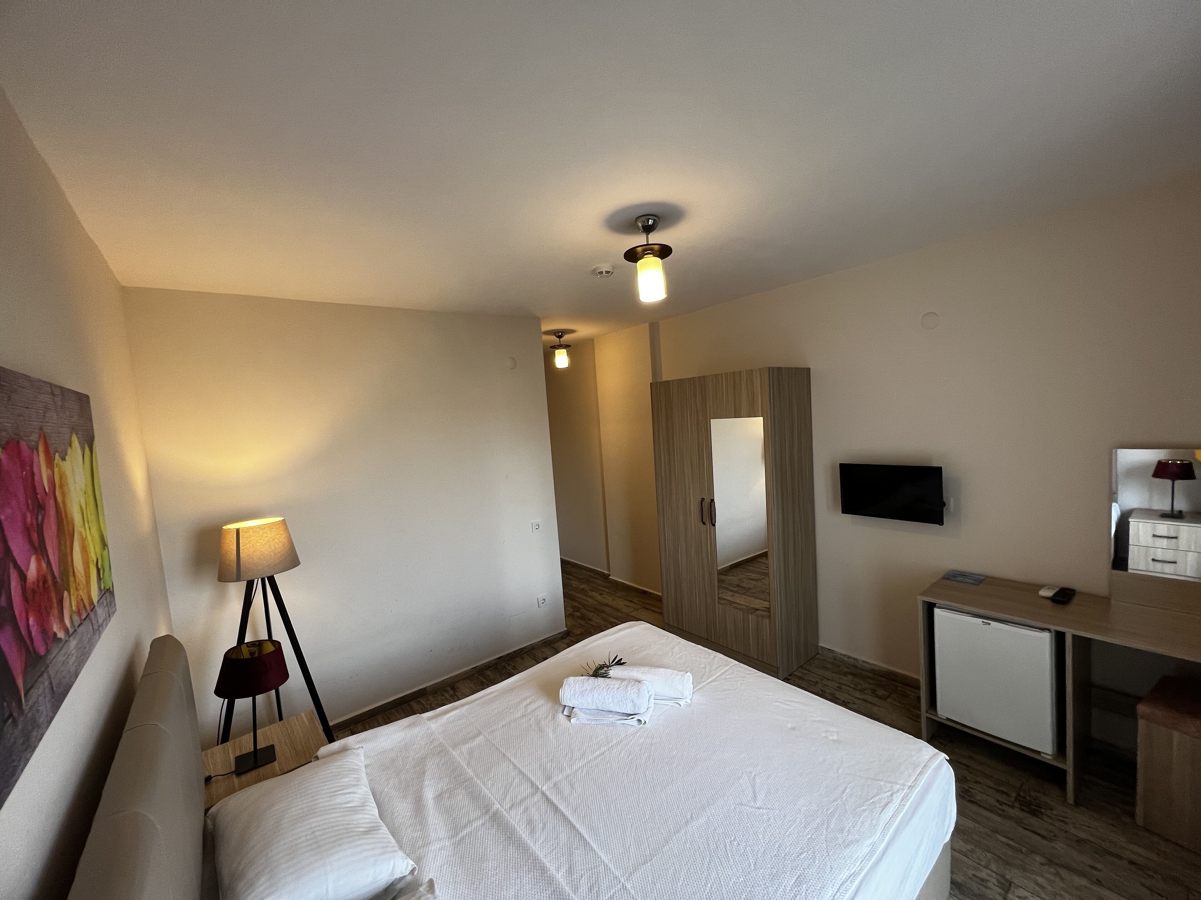 A hotel room with a bed, a desk, a television, and a small refrigerator.